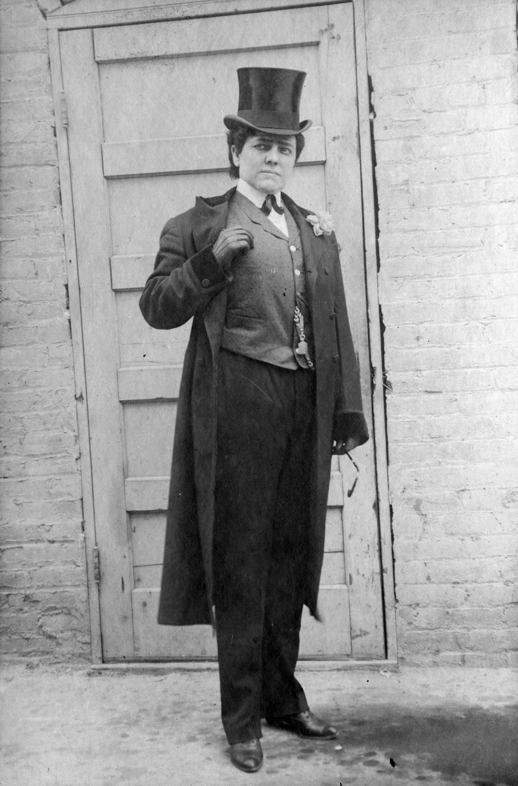 A woman in a top hat and tails poses in front of a door.