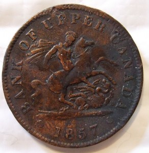 A copper coin that says, Bank of Upper Canada, 1857. A man is pictured in armor on a rearing horse