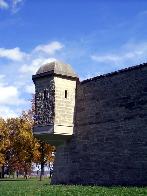 A stone bastion wall with a small turret with slitted windows protruding from the corner.