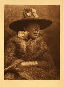 A woman with large, square earlings, a woven hat and blanket, a nose ring, and bracelets.