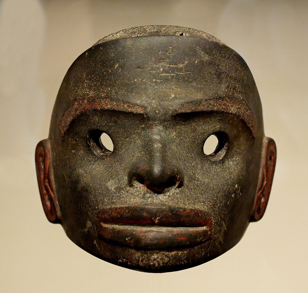A wide rounded stone mask with holes for the eyes. The face has defined ears, eyebrows, a nose, and lips.