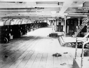 A long row of guns facing out of windows in a boat.