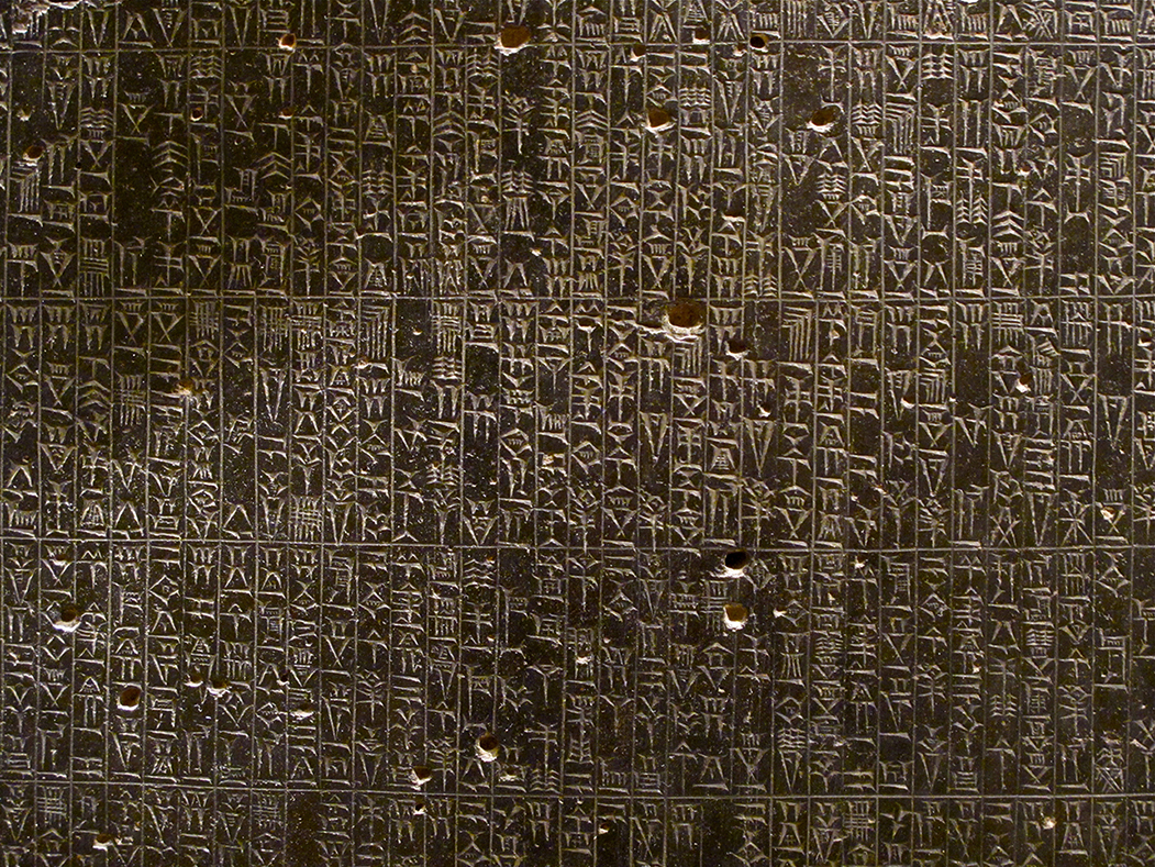 A photo shows a close-up view of the Code of Hammurabi carved into a basalt stele in the Akkadian language, using a cuneiform script.