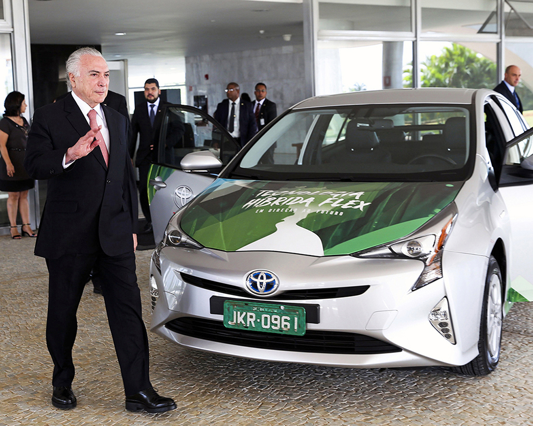 A photo shows Michel Temer waving to the camera as he stands next to a Toyota Prius hybrid electric vehicle at the launch ceremony of the world's first flex hybrid vehicle.