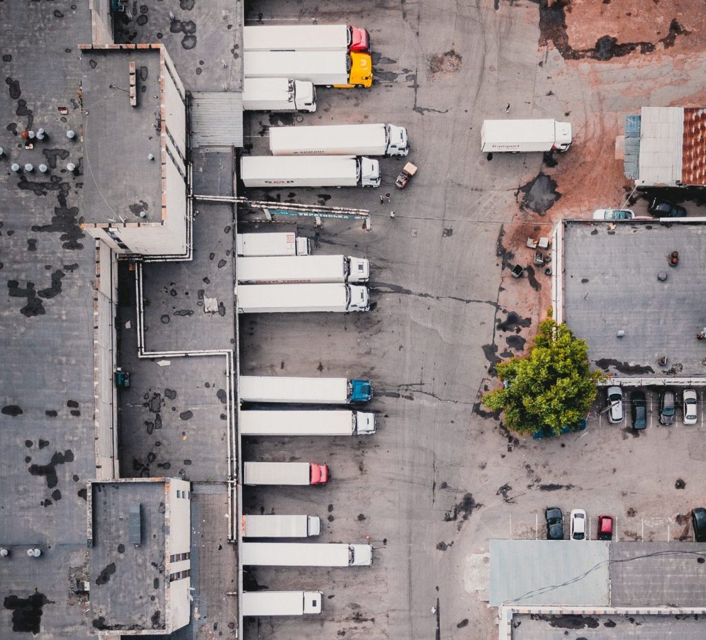 Drone overhead photo of a dozen large trucks being loaded at a warehouse.