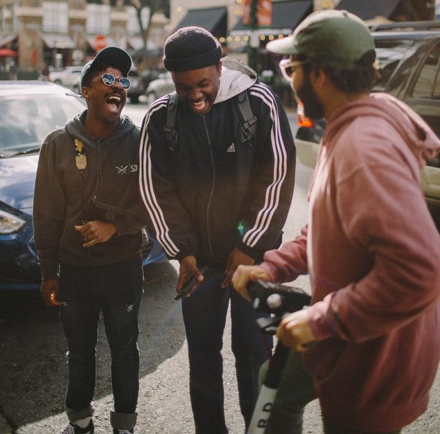 3 men in jackets standing on a street in a city and laughing.