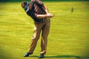 A man mid-swing, playing golf.