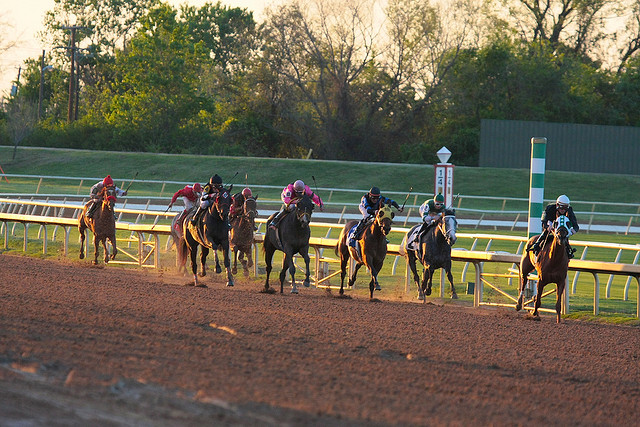 A group of horses racing along a dirt race track.