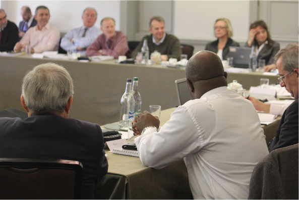 A group of people seated around tables in a meeting room.