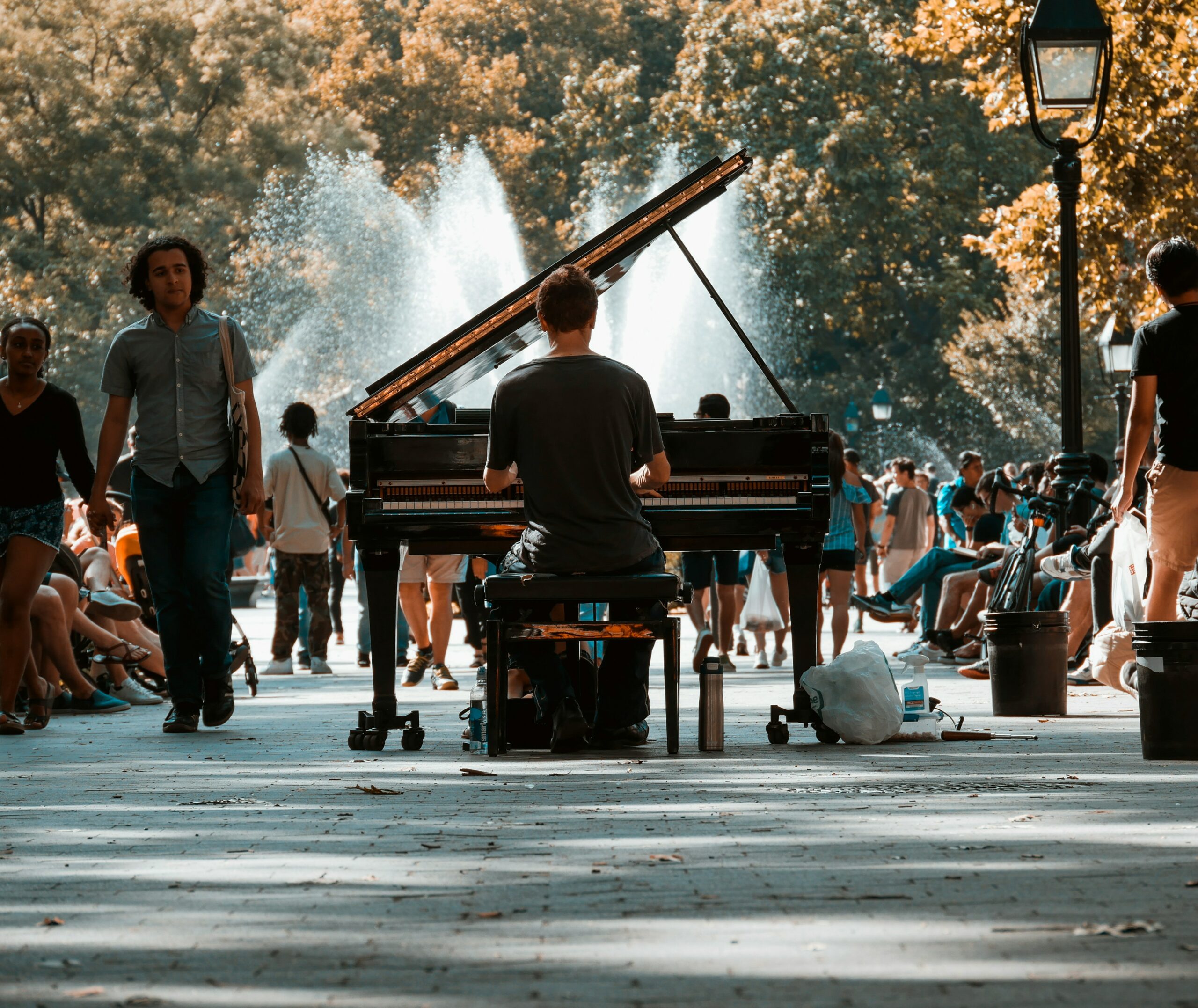 a person plays a grand piano in the middle of a crowded park.