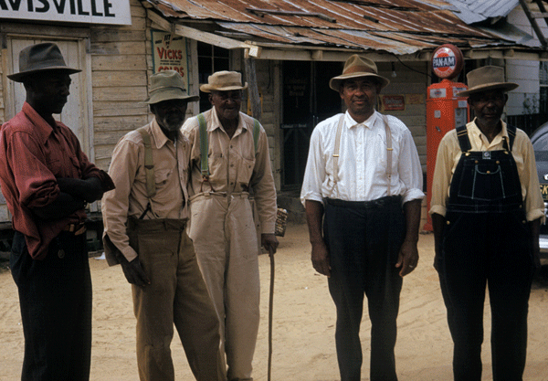 Five older black men standing next to each other. They all have hats, button-up shirts, and either overalls or pants with suspenders.