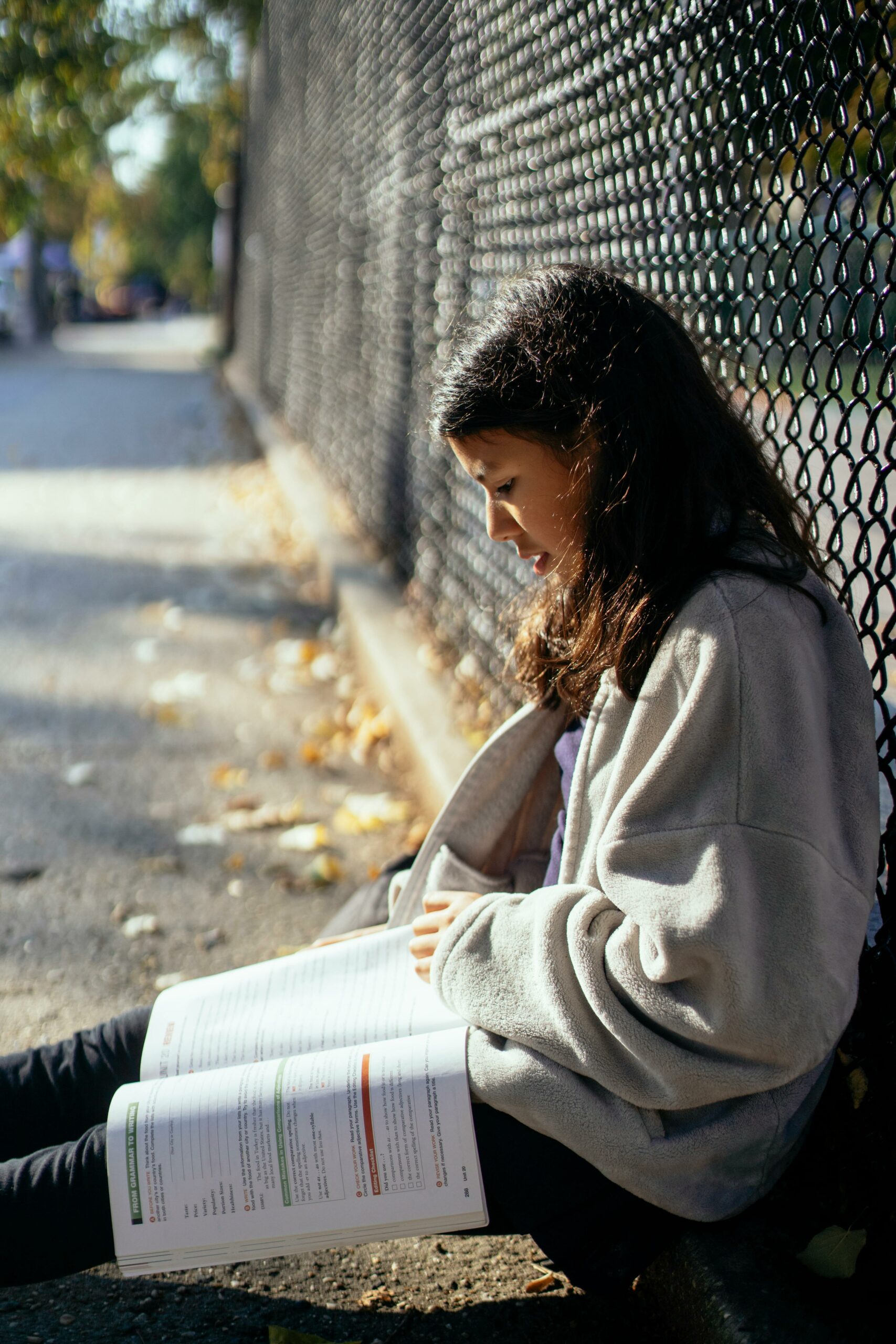 Teenage girl reading textbook on street.