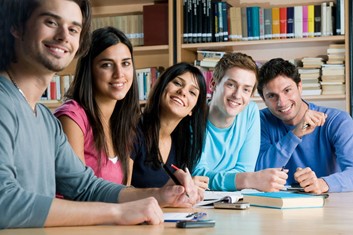 A group of 5 students sitting around a table with books in front of them. They all smile at the camera.