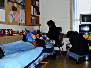 A student with two clones who are reading a textbook, on the computer, and searching through his backpack all at once.