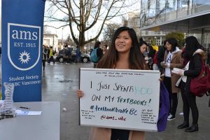 A female student holds up a whiteboard that says she just spent $400 on textbooks.