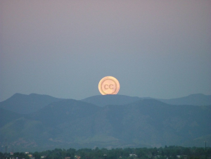 A moon peaking up over distant mountains. The moon has the Creative Commons' CC logo on it.
