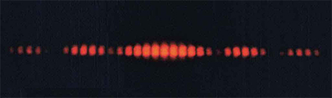 Figure is an image showing red interference pattern on a black background. The central part has brighter lines. The lines are cut off at the top and bottom, seemingly enclosed between two sinusoidal waves of opposite phase.