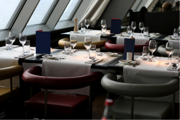 A fancy dining room with white tablecloths, wine glasses, and cushy leather chairs.