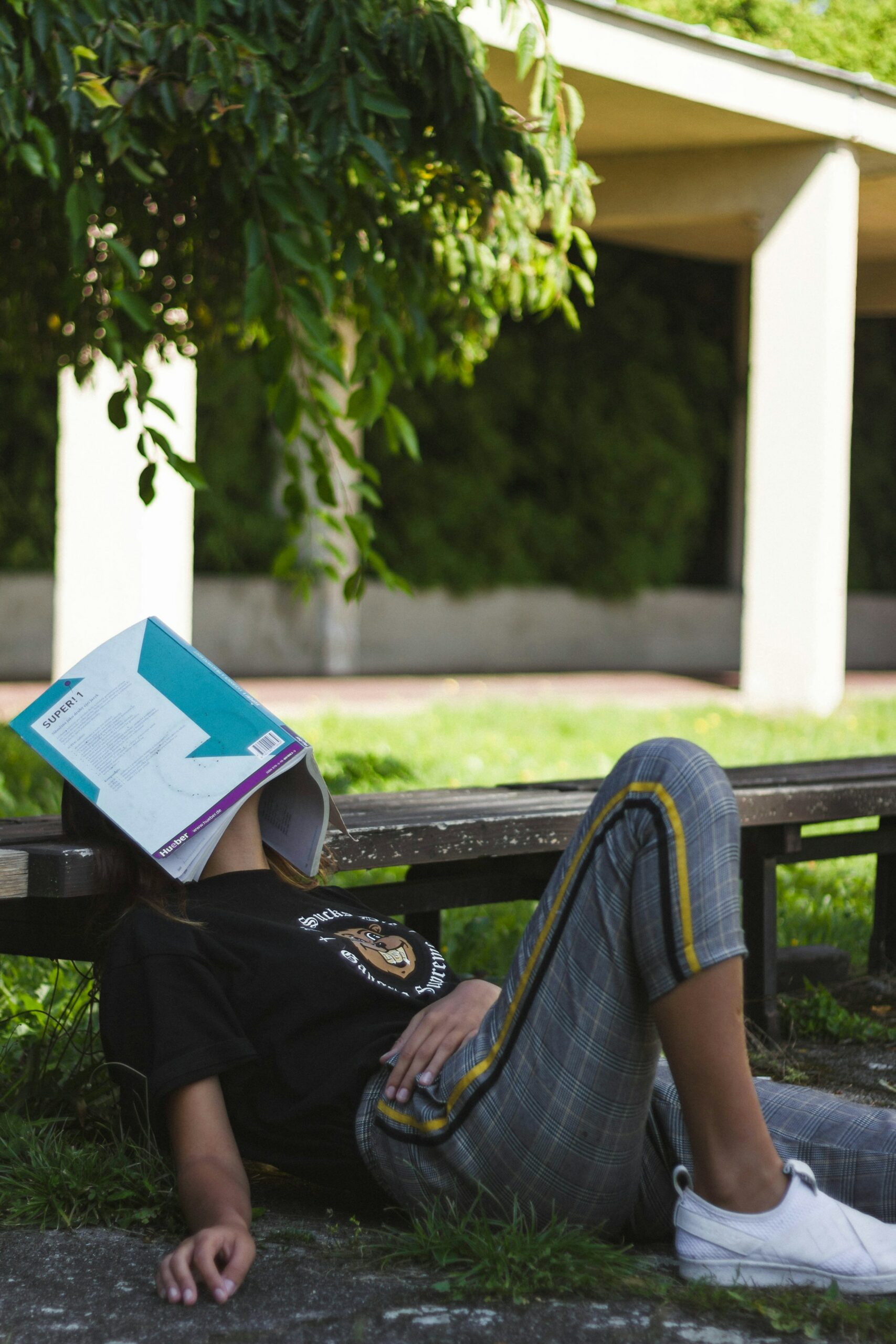 A student lying on the grass relaxing with a book covering their face.