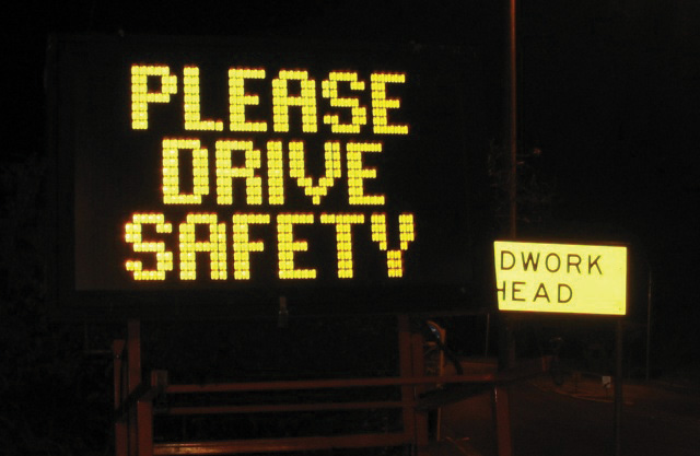 An illuminated road sign that reads: "Please drive safety."